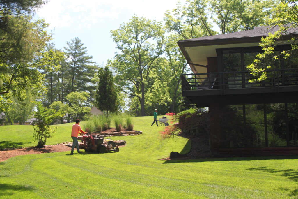 Quiet Village Landscaping crew mowing and maintaining a lush residential lawn in St. Louis with professional equipment. Healthy green sod and mature landscape surround a modern home